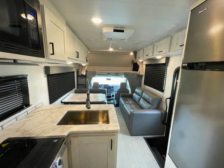 View inside an rv rental, showing kitchen with microwave/sink, dinette, sofa, and overhead bunk area.. Entrada Entrada Motorhome 2022
