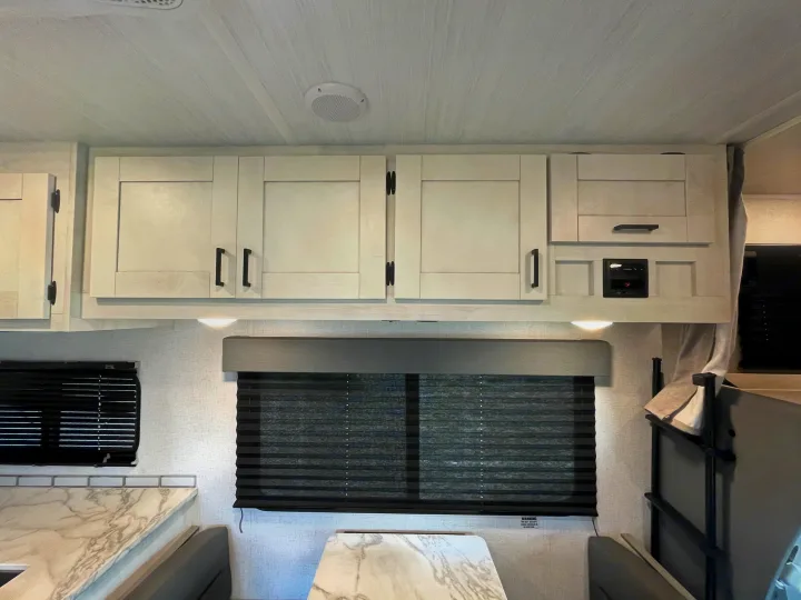 RV rental interior showing bright white overhead cabinets, a dinette area with blinds, and ceiling speaker. Functional and modern.. Entrada Entrada Motorhome 2022