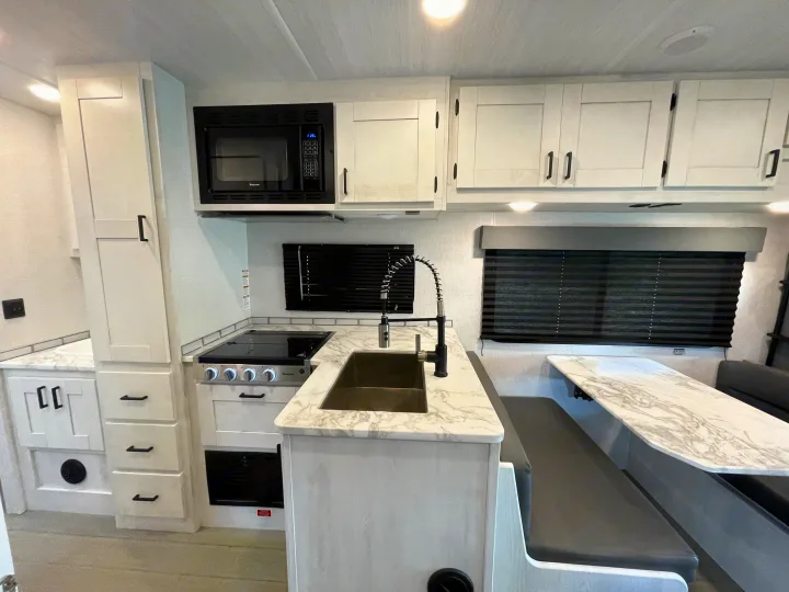 Sleek rv rental kitchen with white cabinets, black appliances, marbled counters, & a cozy dinette booth.. Entrada Entrada Motorhome 2022