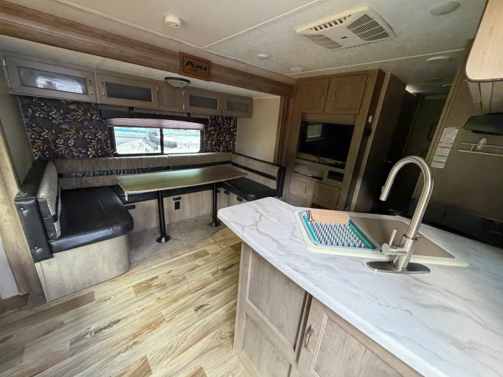 RV rental interior: comfy dinette, kitchen sink, and entertainment unit. Enjoy travel in this well-equipped camper.. Forest River Palomino Puma XLE 2023