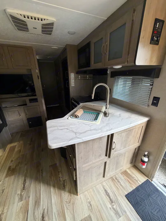 RV rental interior: well-equipped kitchen with sink, microwave, stove, modern cabinets, TV, and wood-look flooring.. Forest River Palomino Puma XLE 2023
