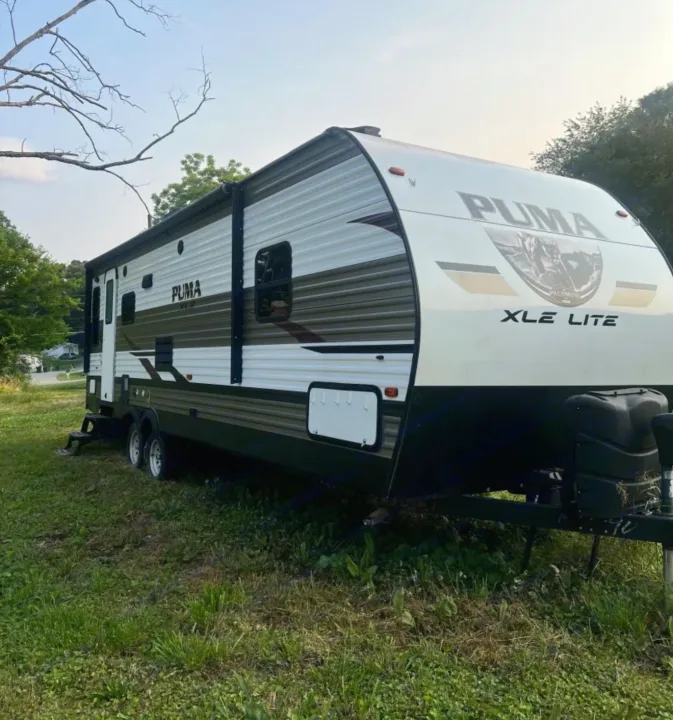Puma XLE Lite RV rental, a white and brown travel trailer, parked outdoors on grass. Ready for your next adventure!. Forest River Palomino Puma XLE 2023