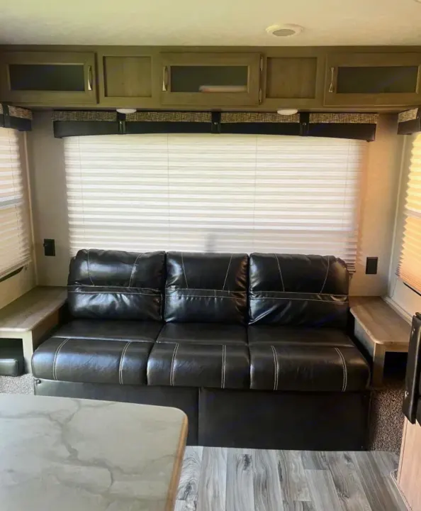 Inside this RV rental: a cozy living area with a black leather sofa, overhead cabinets, window blinds, and wood accents.. Forest River Palomino Puma XLE 2023