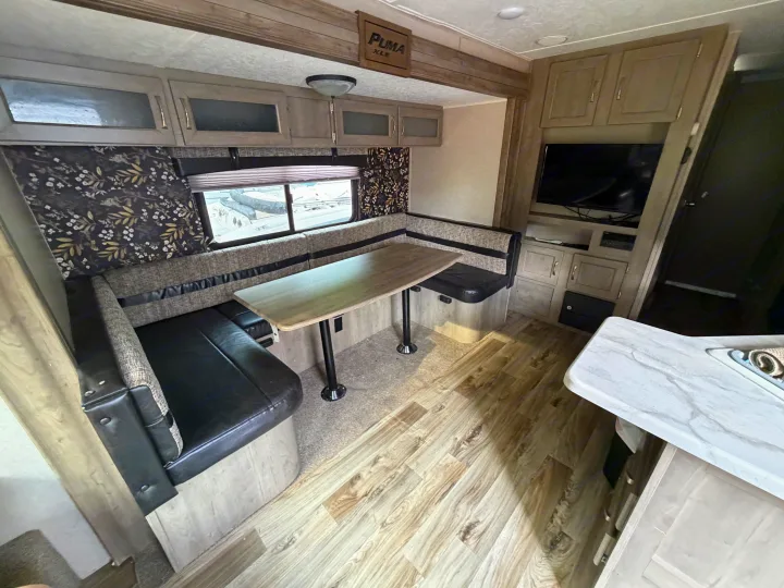 Inside this RV rental, find a light wood dinette with comfy booth seating, overhead storage, and an entertainment center.. Forest River Palomino Puma XLE 2023