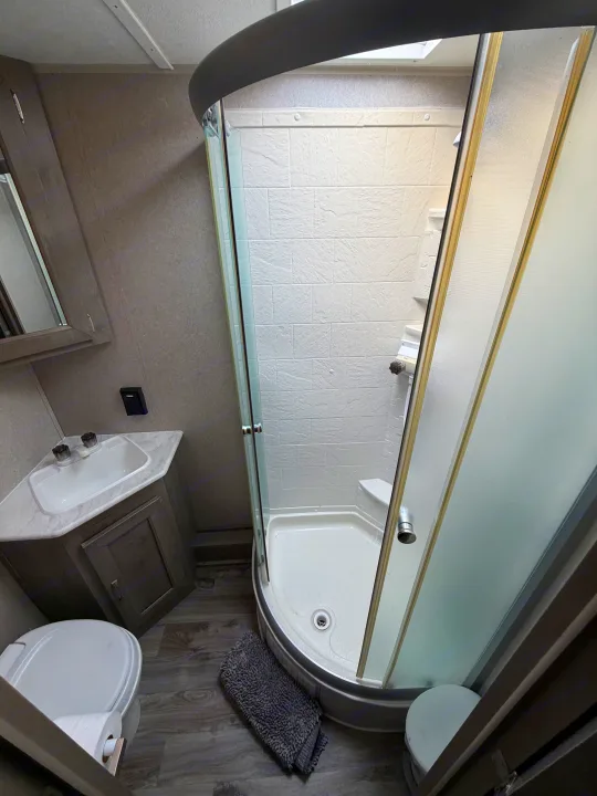 Clean, compact RV rental bathroom with a curved glass shower, toilet, and vanity sink for convenience.. Forest River Palomino Puma XLE 2023