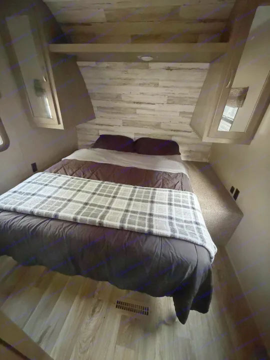 RV rental: A cozy bedroom with a bed, dark bedding, and a plaid blanket. Features plank walls, built-in cabinets, and wood-style flooring.. Forest River Palomino Puma XLE 2023