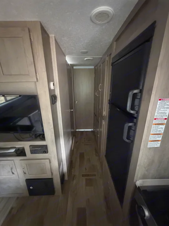 View of an RV rental interior hallway. A refrigerator, TV, and cabinets line the passage leading to a closed door.. Forest River Palomino Puma XLE 2023