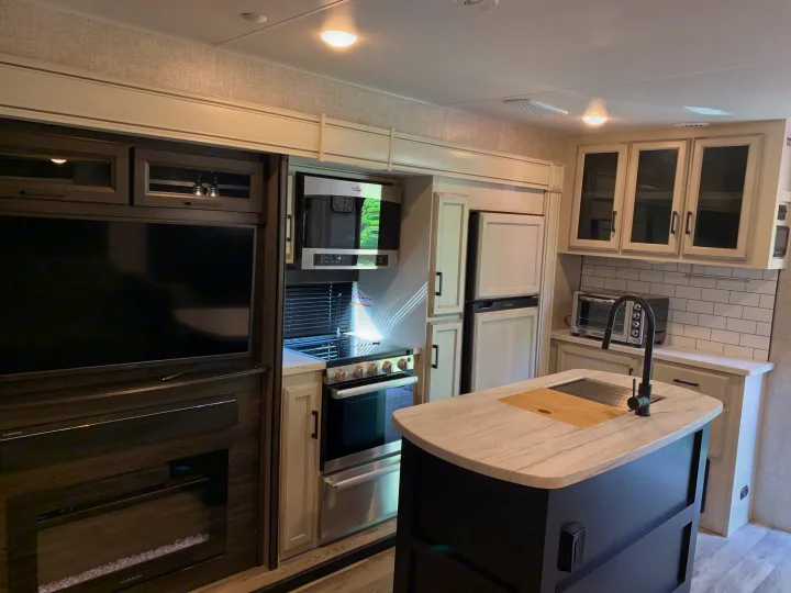 Explore this stylish RV rental kitchen. Features modern appliances, island with sink, TV, and fireplace for a comfy travel experience.. Jayco Eagle HT 2022
