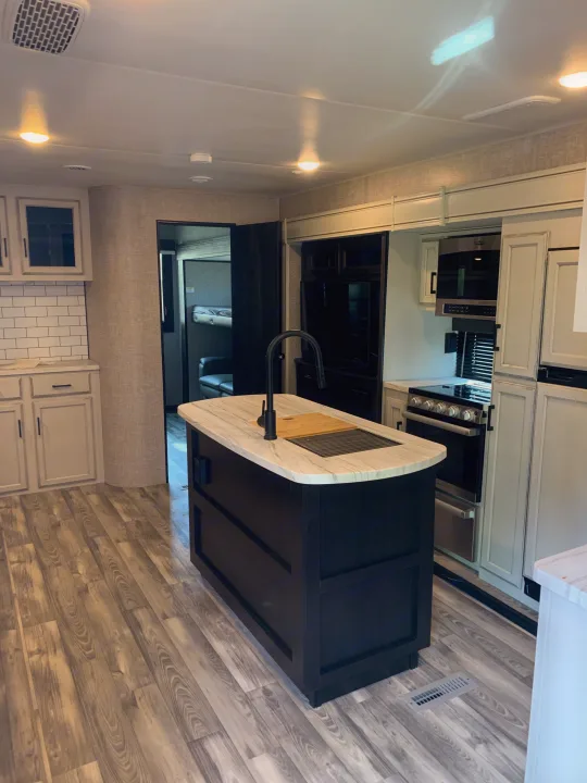 Modern RV rental with a stylish kitchen island, black faucet, light cabinets, wood-look floor, and bunk room access.. Jayco Eagle HT 2022