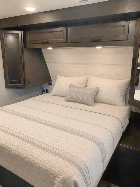 Cozy RV rental bedroom with a striped, quilted bedspread, soft pillows, dark wood cabinets, and a light wood headboard for comfort.. Jayco Eagle HT 2022