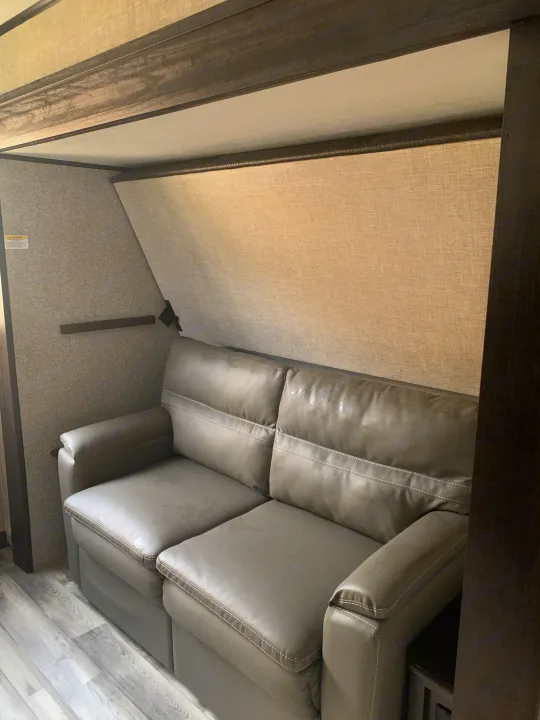 RV rental interior showing a comfortable gray sofa with white stitching below a light-colored, fold-down bunk bed.. Jayco Eagle HT 2022