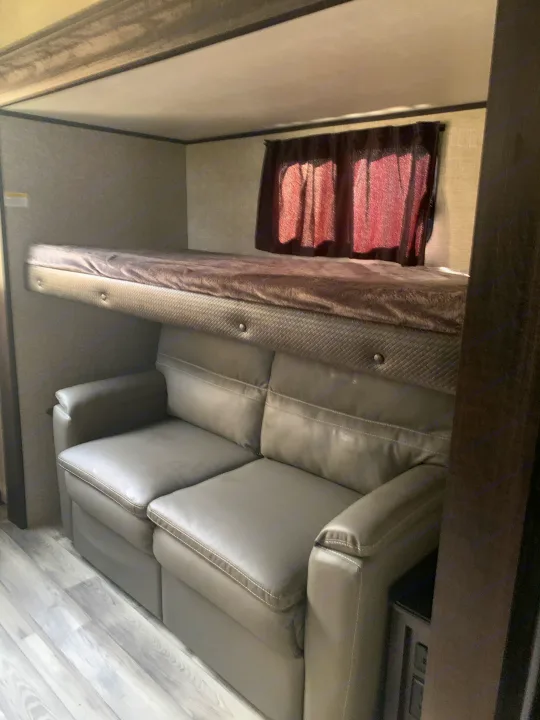 Inside an RV rental: a plush bunk bed sits above a comfortable gray sofa, maximizing space for travel and relaxation.. Jayco Eagle HT 2022