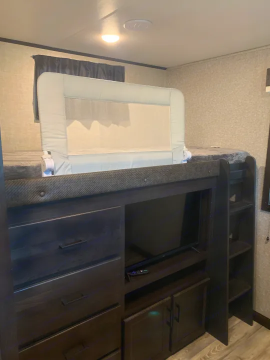Interior of an RV rental: bunk bed with safety rail, TV console with drawers and shelves for comfortable travel.. Jayco Eagle HT 2022