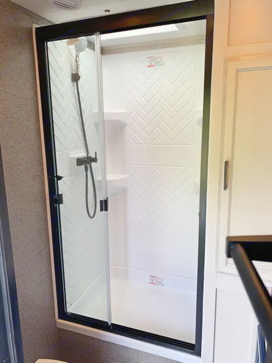 Modern rv rental shower with black-framed glass door, white herringbone walls, and a convenient handheld showerhead for your travels.. Jayco Eagle HT 2022