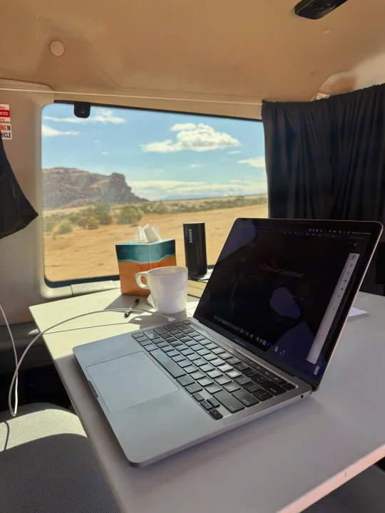 RV rental interior with a laptop, coffee, and Sonos speaker on a table, offering a scenic desert view for remote work.. Ford Econoline 150 2012