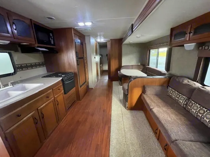 Spacious RV rental interior featuring a kitchen with a stove and sink, a dinette, and a comfortable sofa.. Coachmen Freedom Express 2015