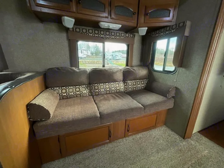 Comfortable RV rental living area with a brown sofa, overhead cabinets, and windows.. Coachmen Freedom Express 2015