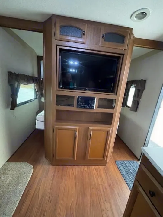 RV rental interior: entertainment center with TV & stereo, wood cabinets. Bedroom & kitchen visible.. Coachmen Freedom Express 2015