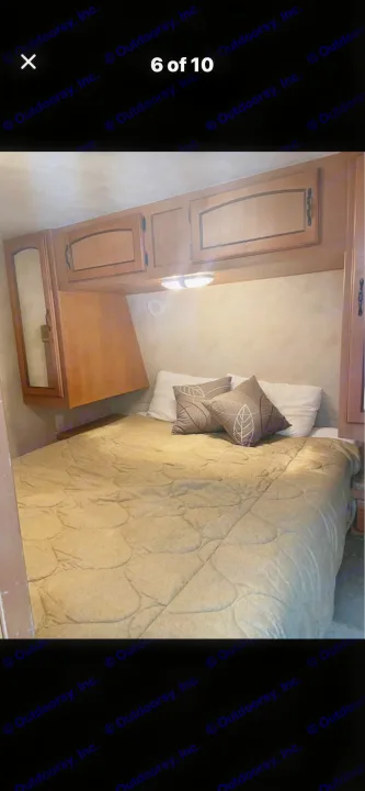 Comfortable RV rental bedroom featuring a cozy bed with patterned pillows, overhead storage, and a bedside light fixture.. Puma Puma 2011