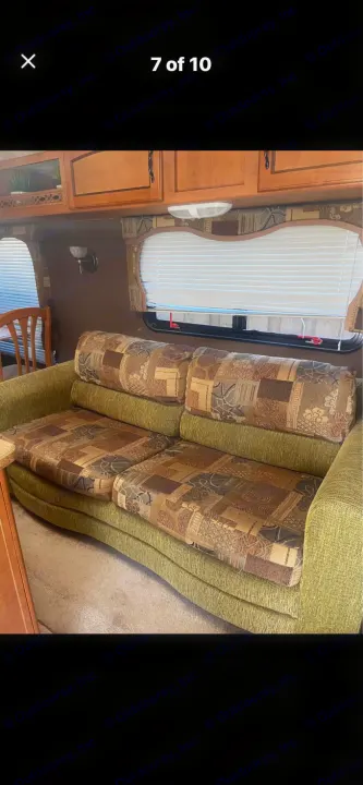 RV rental interior with a green sofa featuring patterned cushions, wooden cabinets, and windows with blinds.. Puma Puma 2011