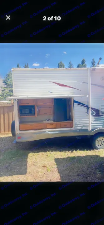 RV rental: Side of travel trailer with an open outdoor kitchen, revealing microwave, fridge, and wood cabinets.. Puma Puma 2011