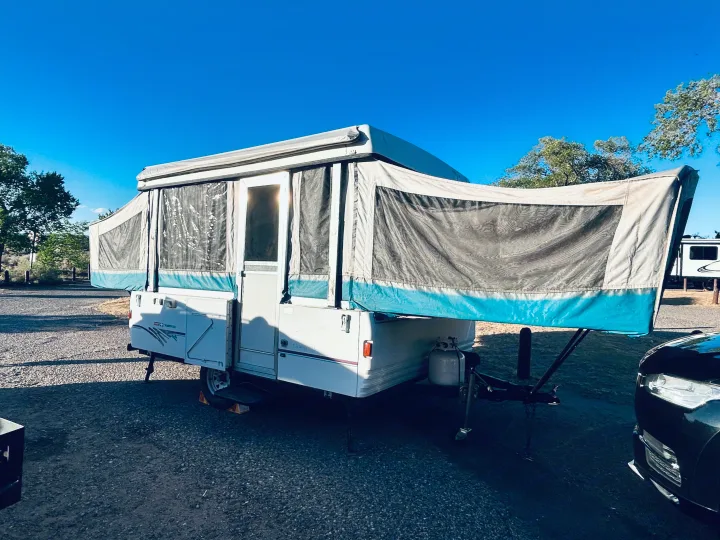 An RV rental, a pop-up camper, fully deployed under a clear blue sky at a gravel campsite. Ready for adventure.. Coleman Destiny Santa Fe 1996