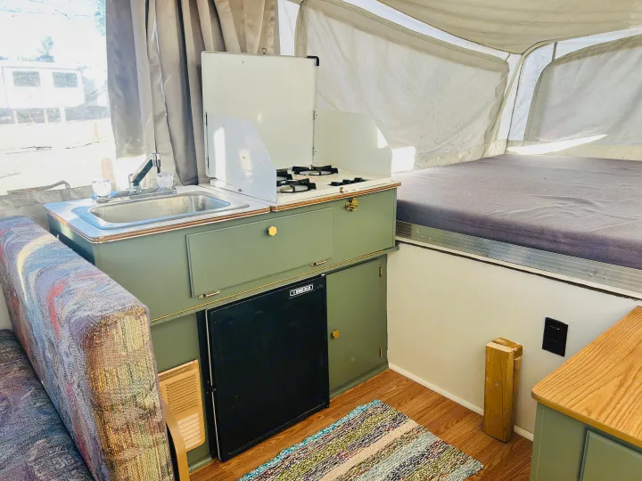 RV rental pop-up camper interior: sage green kitchenette with sink, stove, fridge, upholstered seating, and a bed.. Coleman Destiny Santa Fe 1996