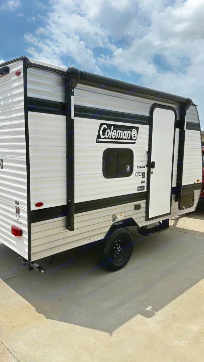 This Coleman travel trailer, ideal for an rv rental, is parked outside on a sunny day. Its white and grey exterior and awning hint at outdoor adventures.. Keystone RV 13B travel Trailer 2026