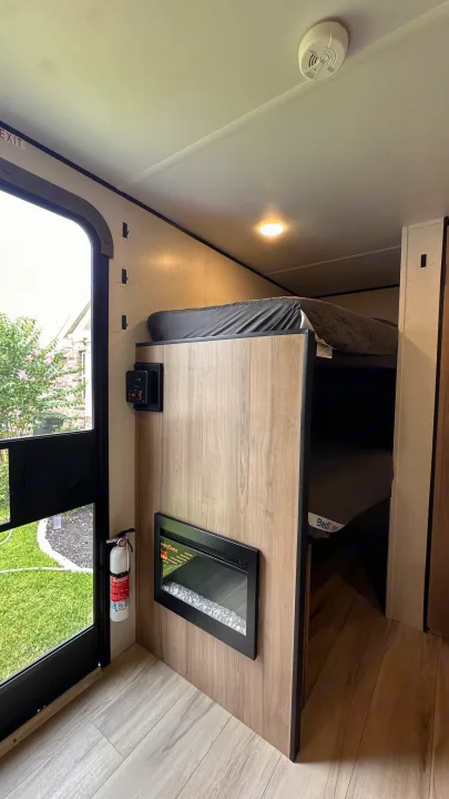 RV rental interior features bunk beds, a wall-mounted electric fireplace, and controls. Safety includes an extinguisher by the exit.. Keystone RV 13B travel Trailer 2026