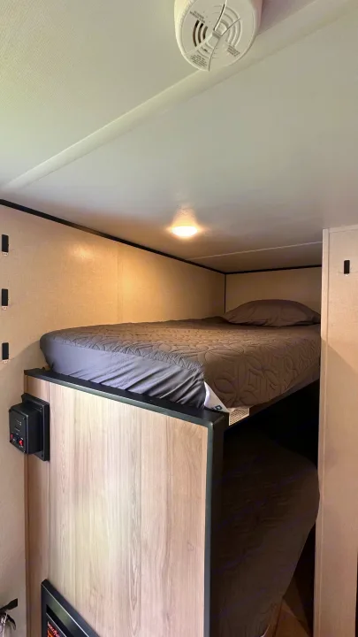 Cozy bunk beds in an RV rental, featuring gray quilted bedding, a ceiling light, and a safety detector on the ceiling.. Keystone RV 13B travel Trailer 2026