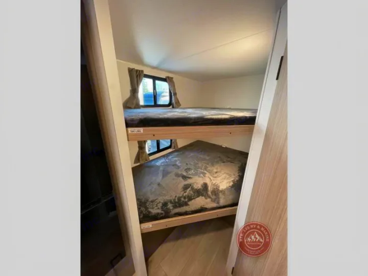 RV rental interior features bunk beds for extra sleeping space. Two bunks, visible windows, and light wood tones define this cozy area.. KZ Sportsmen Select 2026