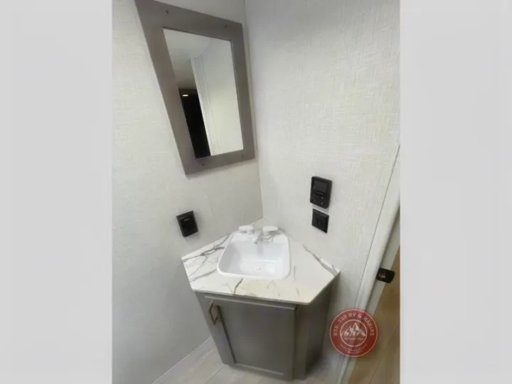 This RV rental bathroom offers a modern, compact vanity with a white sink, marble-look counter, gray cabinet, and framed mirror.. KZ Sportsmen Select 2026