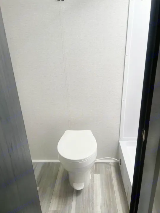 This rv rental bathroom features a white toilet, light grey walls, and a wood-look floor, with a glimpse of the shower.. Keystone RV Springdale 2024