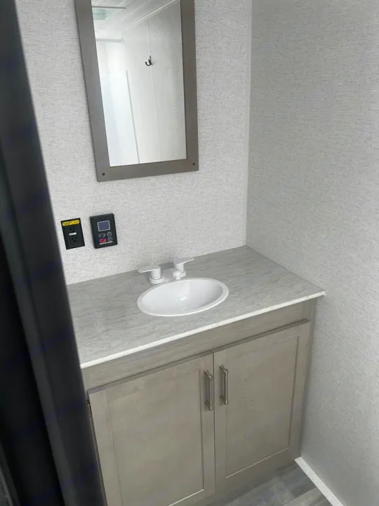RV rental bathroom featuring a gray vanity with sink, mirror, power outlet, and control panel on textured walls.. Keystone RV Springdale 2024