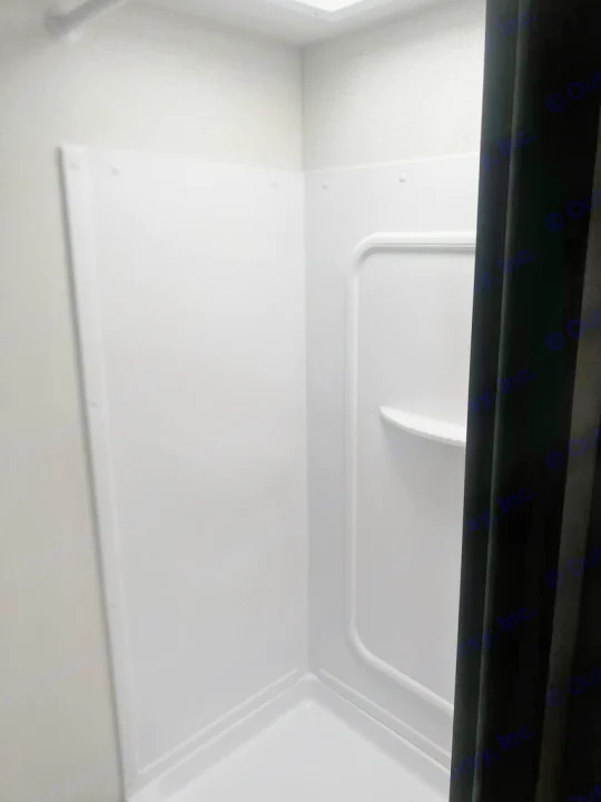 Compact, clean shower in this RV rental, featuring white panels, a corner shelf, and overhead lighting for your trip.. Keystone RV Springdale 2024