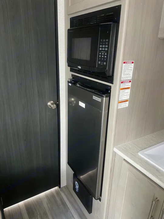RV rental kitchen: A built-in black microwave is mounted above a slim, stainless steel Everchill refrigerator, optimizing space.. Keystone RV Springdale 2024
