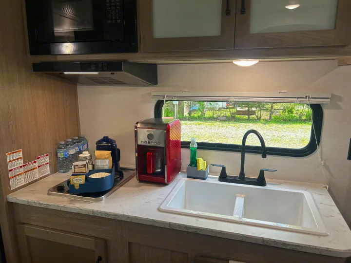 Compact RV rental kitchen with a coffee maker, sink, microwave, and stovetop, ready for use by travelers.. Gulf Stream Grand River 25BH 2026