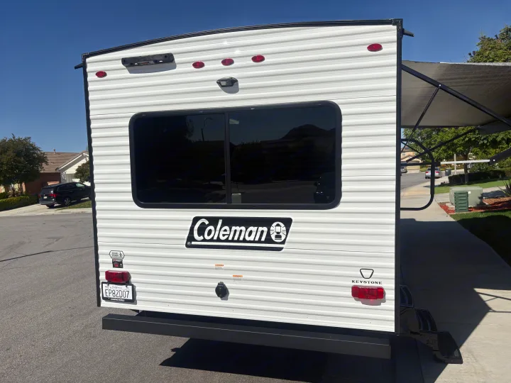 Rear view of a Coleman RV rental / travel trailer, showing license plate, tail lights, and an awning.. Keystone RV Other 2026