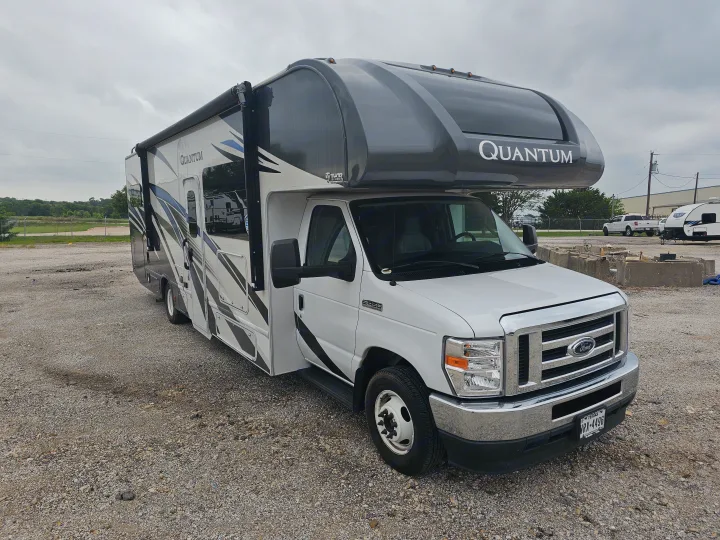 White & gray Thor Quantum Class C RV rental on a Ford E-350 chassis, parked on gravel under cloudy skies, ready for adventure.. Thor Quantum 2023