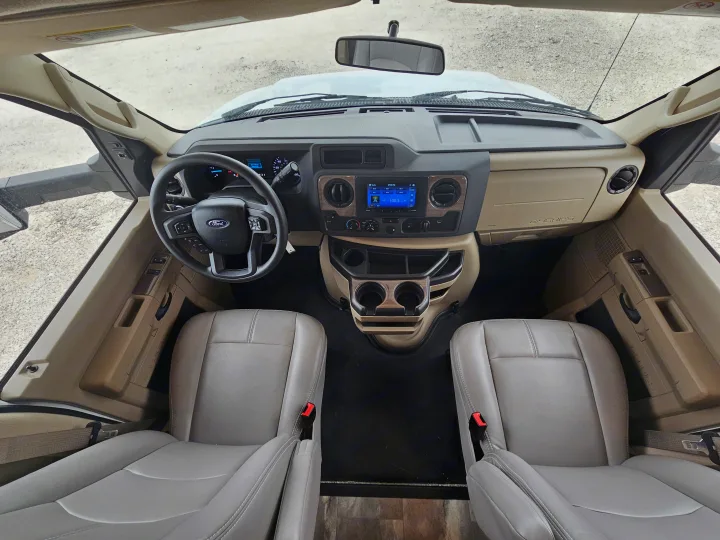 Top-down view of an RV rental cockpit with beige interior, showing Ford steering wheel, dashboard, and front seats.. Thor Quantum 2023