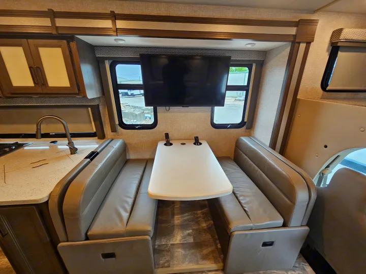 This RV rental interior features a dinette with bench seats, a wall-mounted TV, and a kitchen counter with a sink.. Thor Quantum 2023