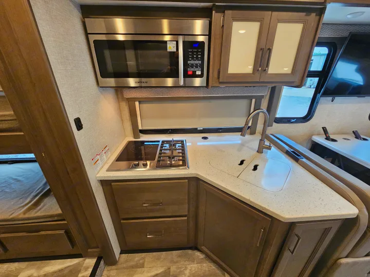 Explore this modern rv rental kitchen with microwave, stove, sink, cabinets, bunk beds & a dinette area visible.. Thor Quantum 2023