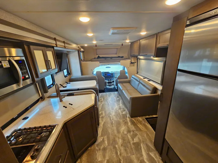 Interior of a modern rv rental with a full kitchen, dining area, living space, refrigerator, and cockpit view.. Thor Quantum 2023