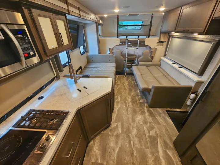 Spacious rv rental interior featuring a modern kitchen with stove/microwave, comfy sofas, and an overhead bed, ideal for travel.. Thor Quantum 2023