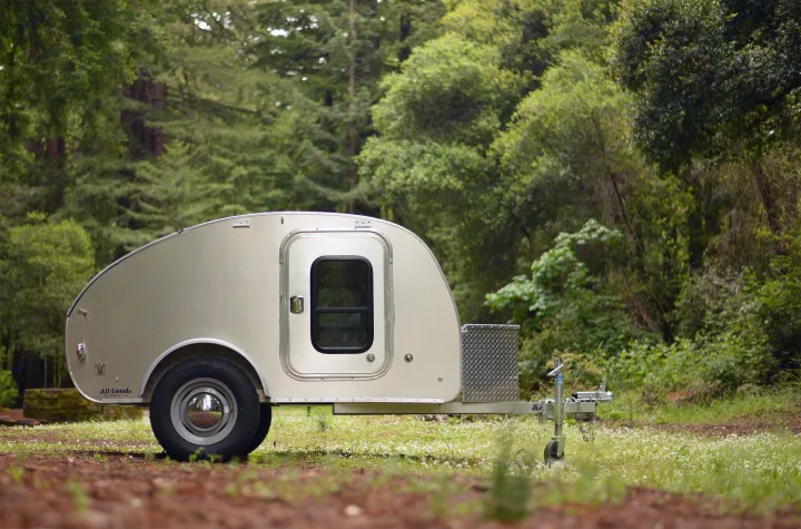 A silver 'All Good' teardrop trailer for rv rental is parked in a lush forest. Great for compact camping adventures.. All Good Equipment Company Teardrop Trailer 2026
