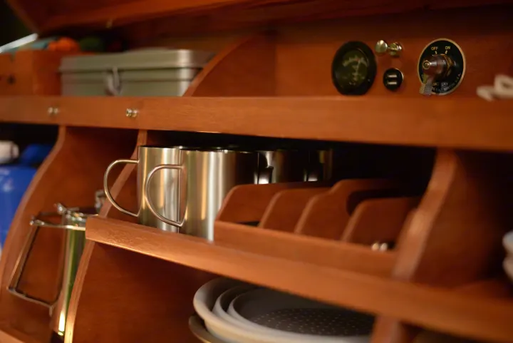 Cozy RV rental interior featuring organized wooden shelving with stainless steel mugs, battery controls, and USB ports.. All Good Equipment Company Teardrop Trailer 2026