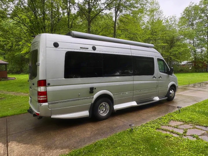 Silver Mercedes Sprinter RV rental, a spacious camper van parked on a driveway with lush green surroundings.. Winnebago Era 2017