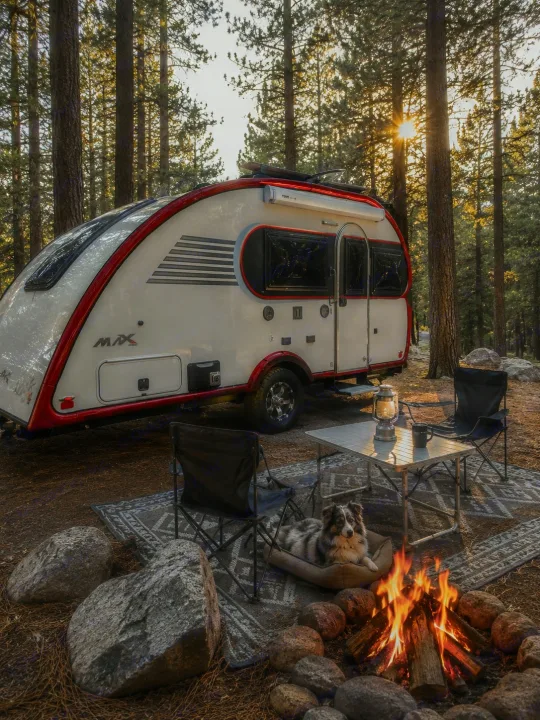 Experience nature! Teardrop RV rental parked in a sun-dappled forest, with a cozy campfire & dog on a rug.. Liberty Outdoors Little Guy 2018