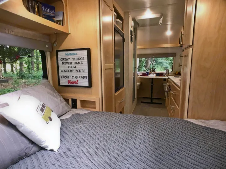 Cozy RV rental interior with a comfy bed, kitchen, and scenic window view. A "travel" quote adds inspiration.. Liberty Outdoors Little Guy 2018