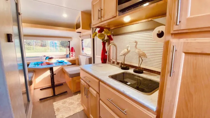 Cozy RV rental kitchen & dining area, featuring wood cabinets, bright decor, and ample light. Ready for travel!. Liberty Outdoors Little Guy 2018